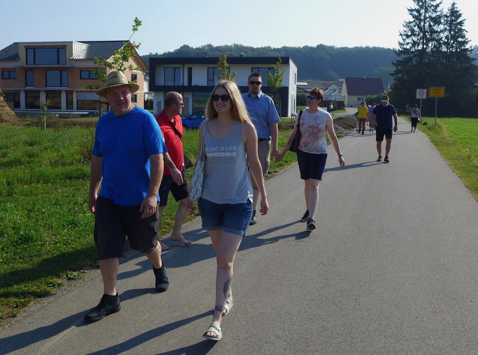 Deltakerne spaserer i solskinn på en markvei i utkanten av byen, i bakgrunnen nybygg og skogkledde åser