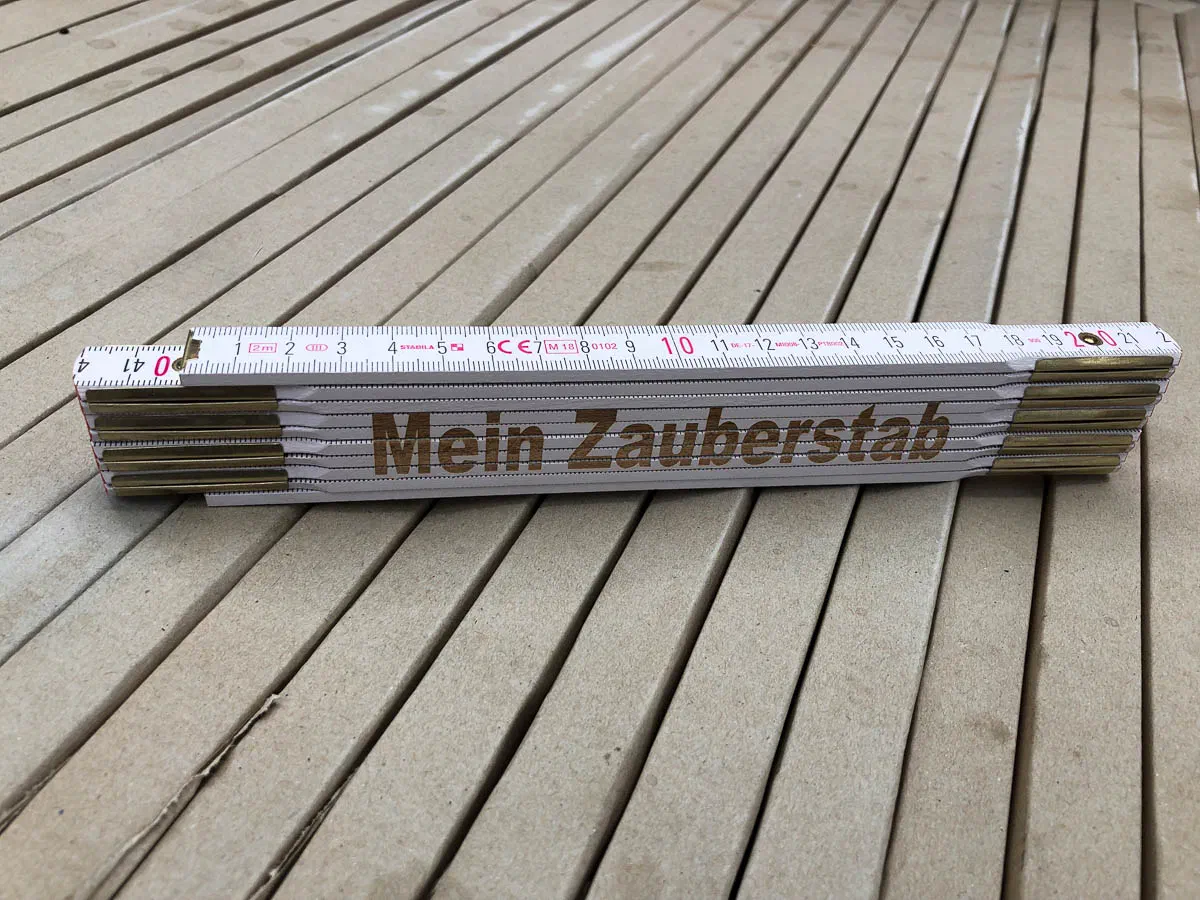 Folded white wooden folding ruler with brass fittings and the inscription “Mein Zauberstab” (my magic wand)